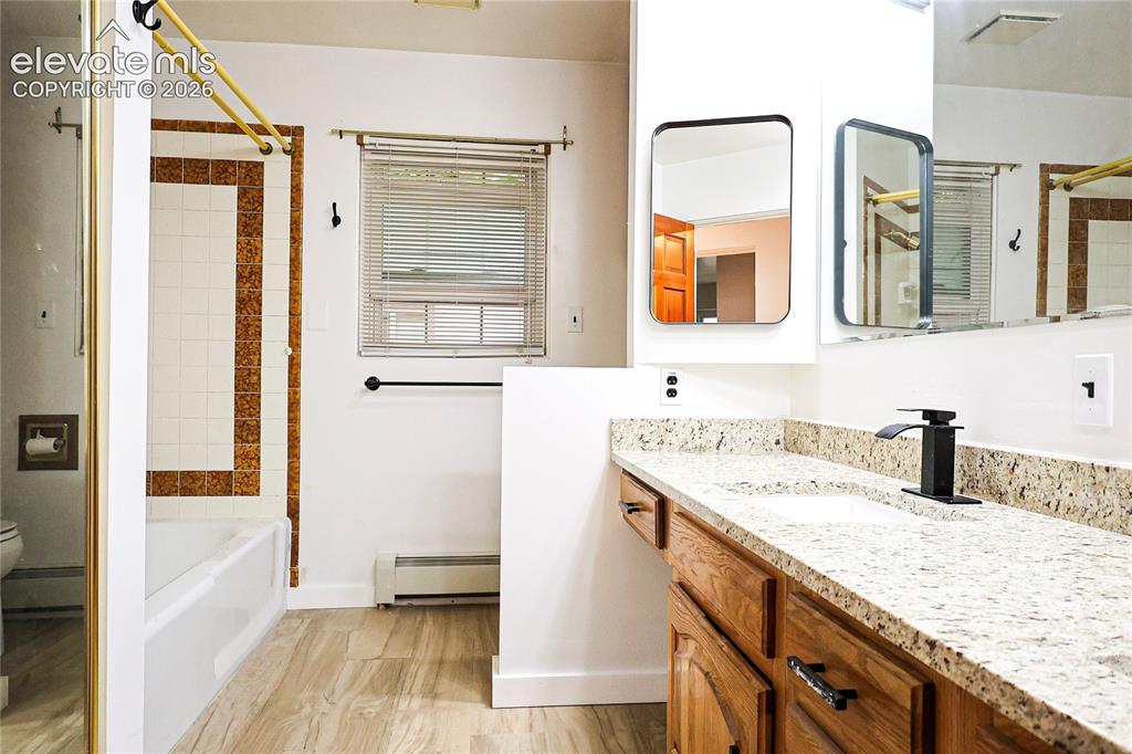 Image 20 of 40: Wood-finish flooring, white bathtub with decorative tile surround, function