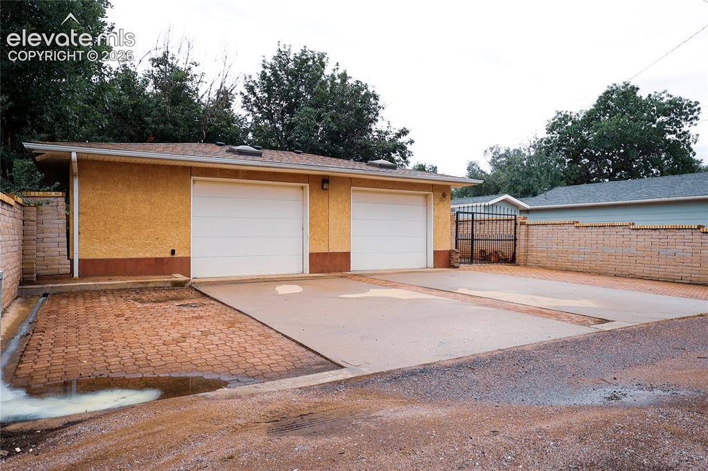 Image 40 of 40: Spacious driveway with herringbone brick paving and concrete apron, complem