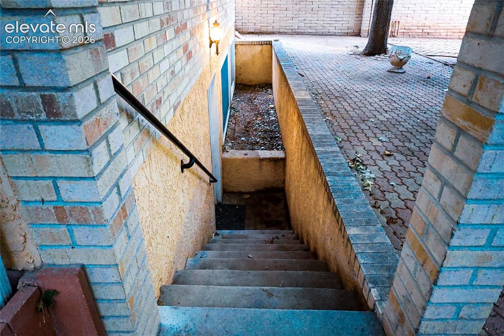 Image 5 of 40: Brick and stucco exterior with concrete stairs, a metal handrail, and a pav