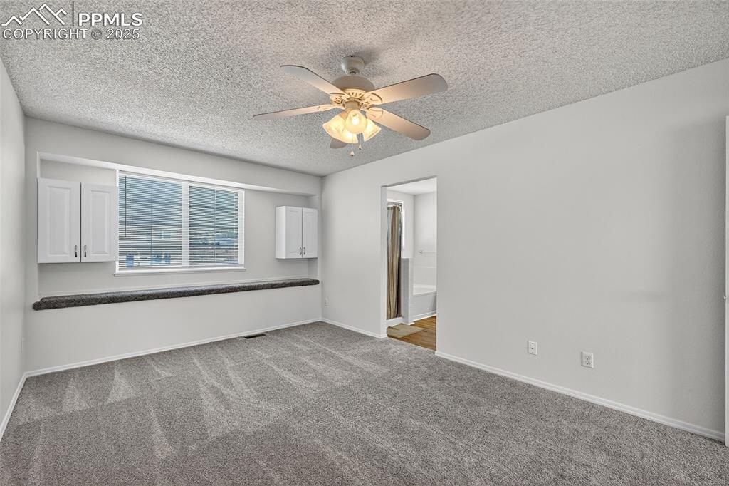 Image 18 of 30: Primary bedroom with carpet, a textured ceiling, and a ceiling fan, entry t