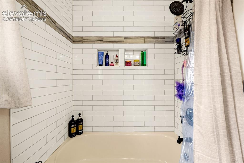 Image 13 of 30: Shower surround featuring white subway tile, a neutral-toned decorative acc