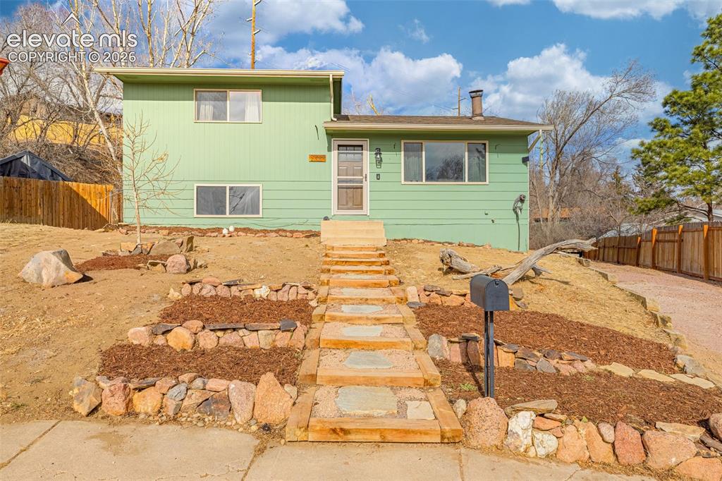 Image 2 of 30: Split-level exterior featuring light green siding, a timber-framed flagston