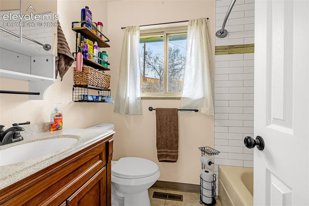 Image 24 of 30: Bathroom featuring a wood-finish vanity with a stone-composite countertop,