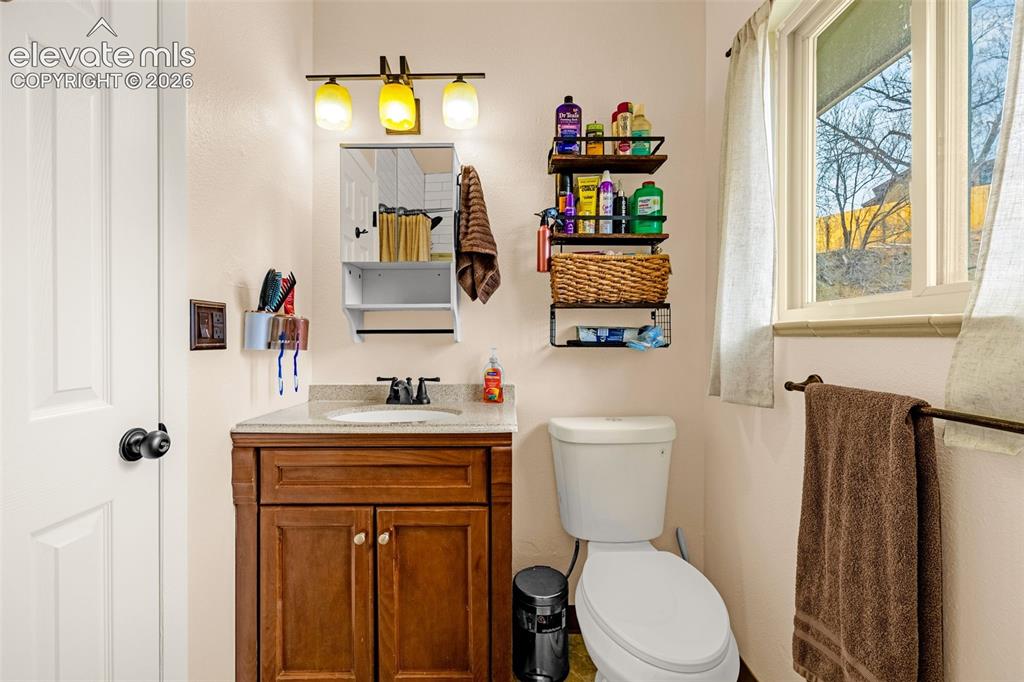 Image 25 of 30: Wood-finish vanity with a stone-composite countertop, drop-in sink, dark-fi
