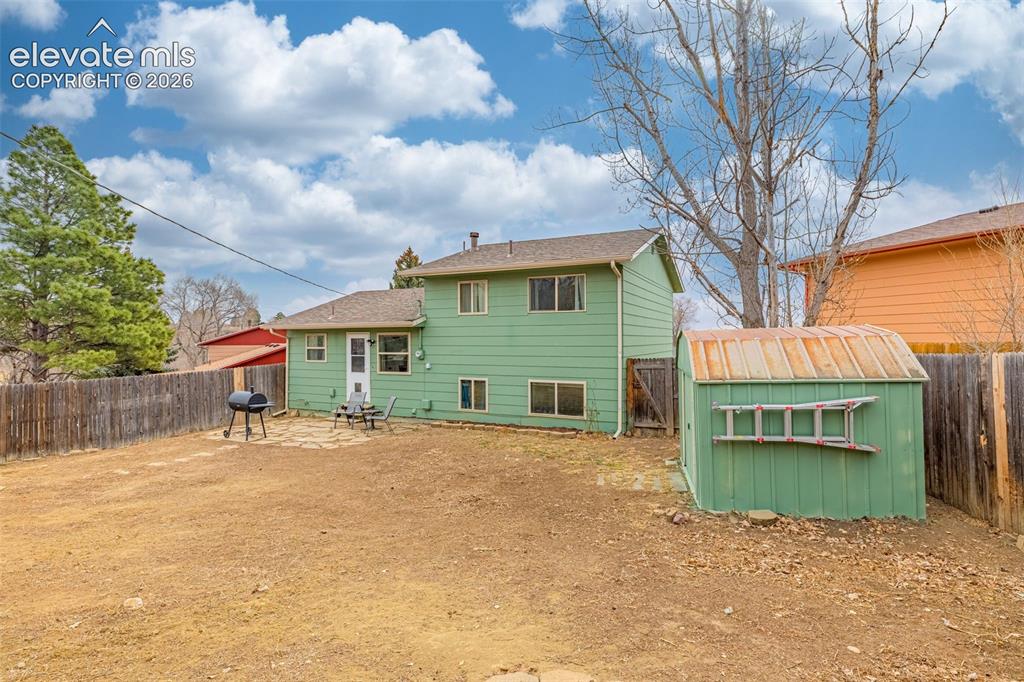 Image 28 of 30: Rear exterior featuring green horizontal lap siding, a flagstone patio, a m
