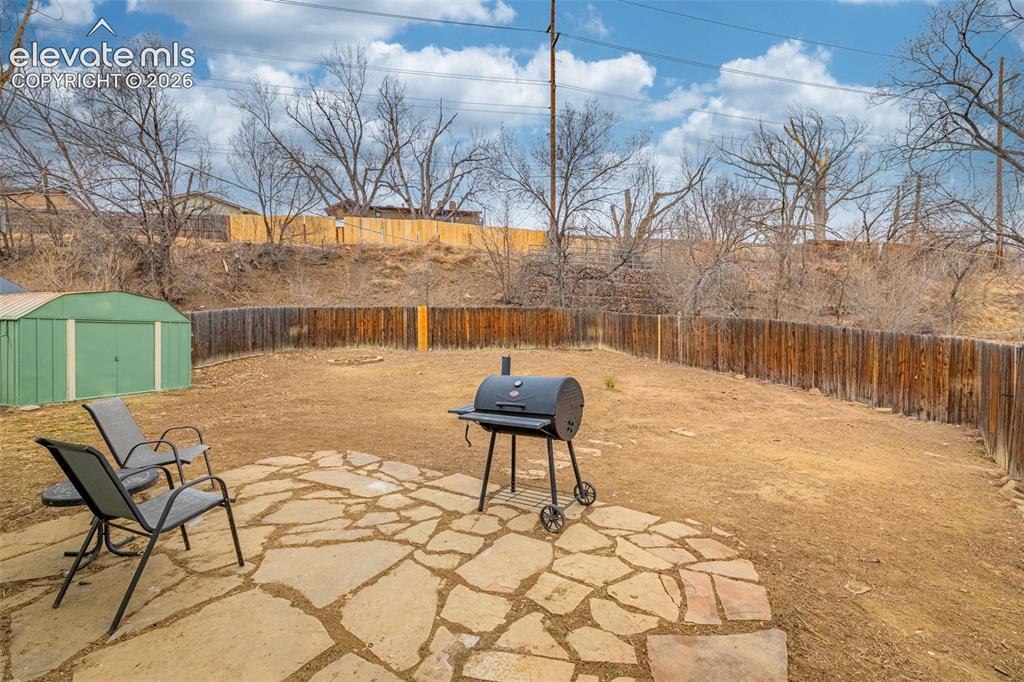 Image 29 of 30: Backyard featuring a stone paver patio, full wood fencing, and a detached m