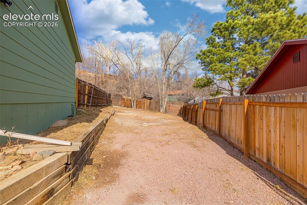Image 30 of 30: Gravel side yard featuring a timber retaining wall and vertical wood privac