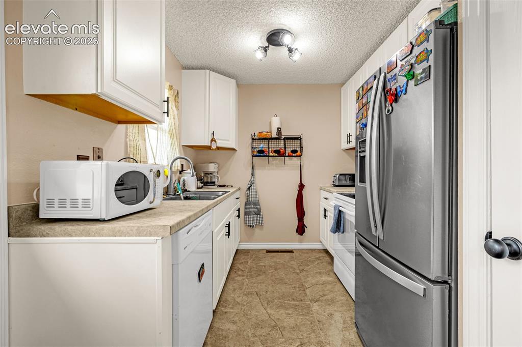 Image 8 of 30: Kitchen featuring white cabinetry with black hardware, stainless steel refr