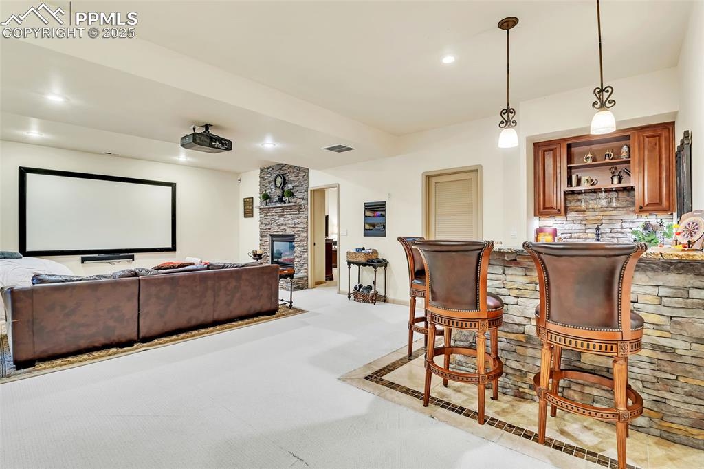 Image 37 of 45: Cinema room featuring a stone fireplace, light carpet, indoor bar, visible 