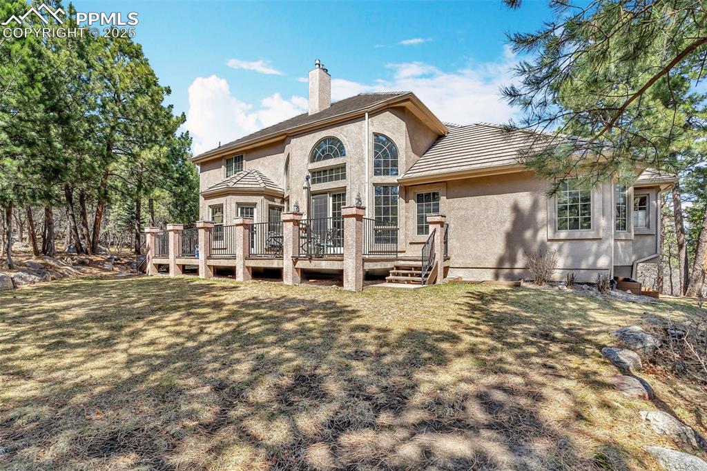 Image 42 of 45: Rear view of property featuring a chimney, a lawn, a tiled roof, stucco sid
