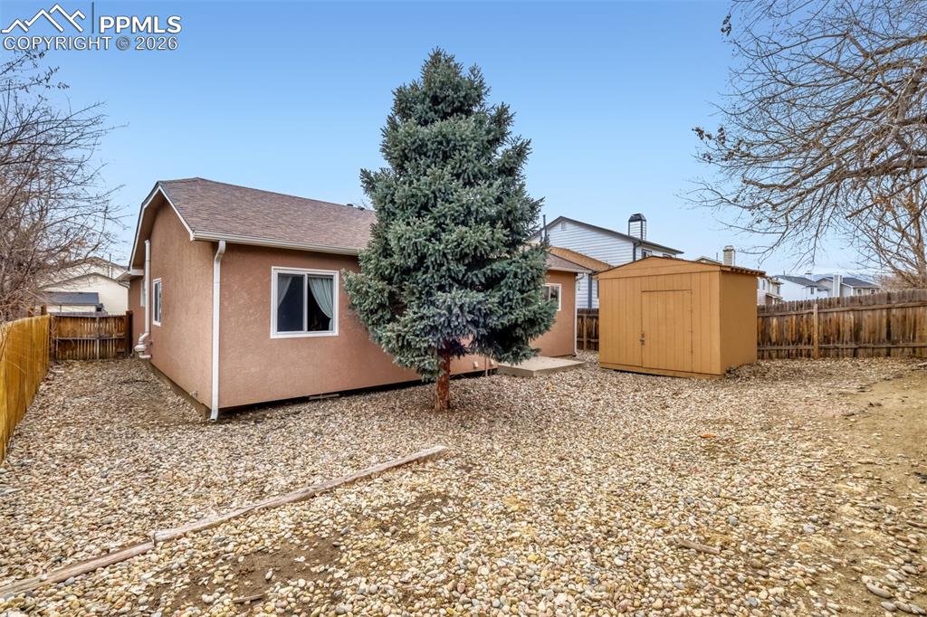 Image 25 of 27: Back of house featuring a fenced backyard, a storage unit, and stucco sidin