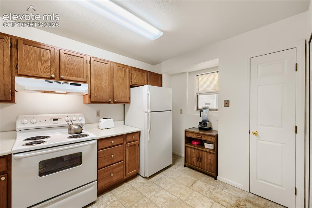 Image 16 of 37: Kitchen featuring wood cabinetry, white appliances, durable tile flooring, 