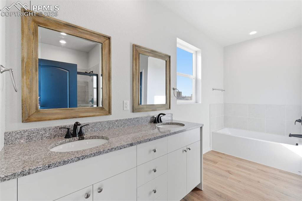 Image 19 of 30: Bathroom with light wood-style flooring, double vanity, a garden tub, a sta