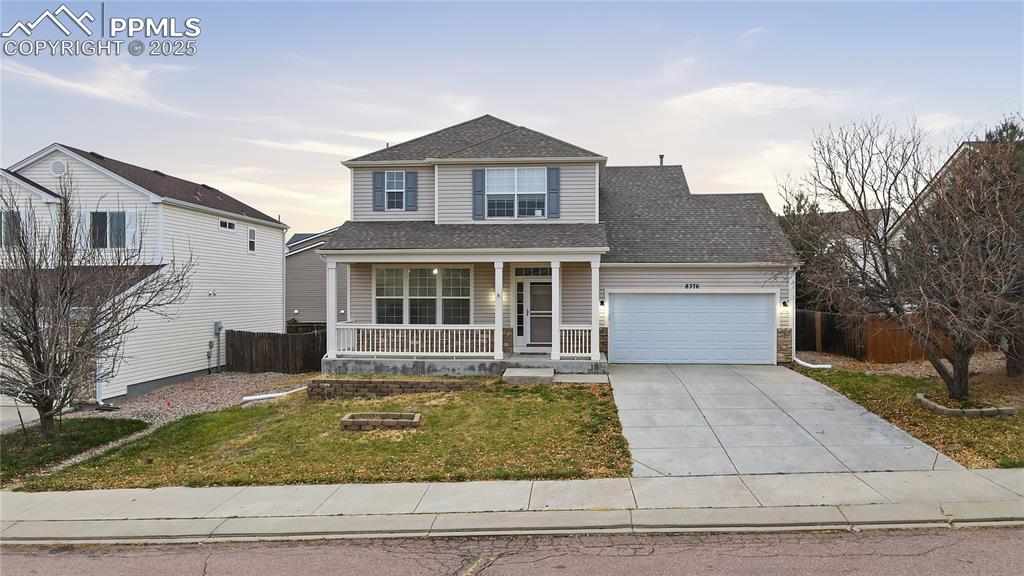 Caption: Traditional-style home featuring a porch, driveway, roof with shingles, and an attached garage