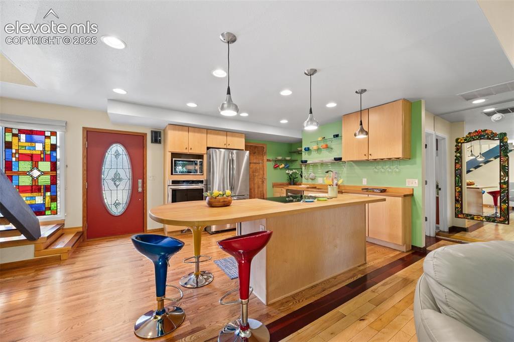 Image 6 of 48: Open-concept kitchen featuring light wood cabinetry, stainless steel applia