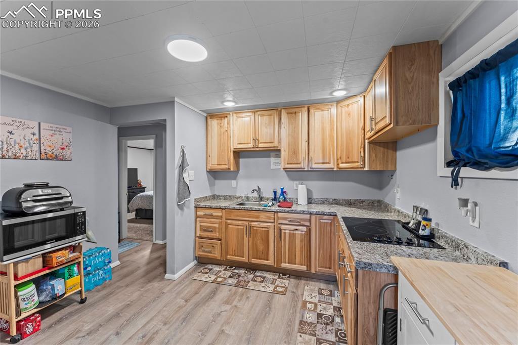 Image 26 of 47: Basement kitchen featuring wood-finish cabinetry, granite-patterned counter