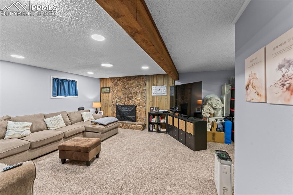 Image 37 of 47: Carpeted living space featuring a stone-clad fireplace with a black grate, 