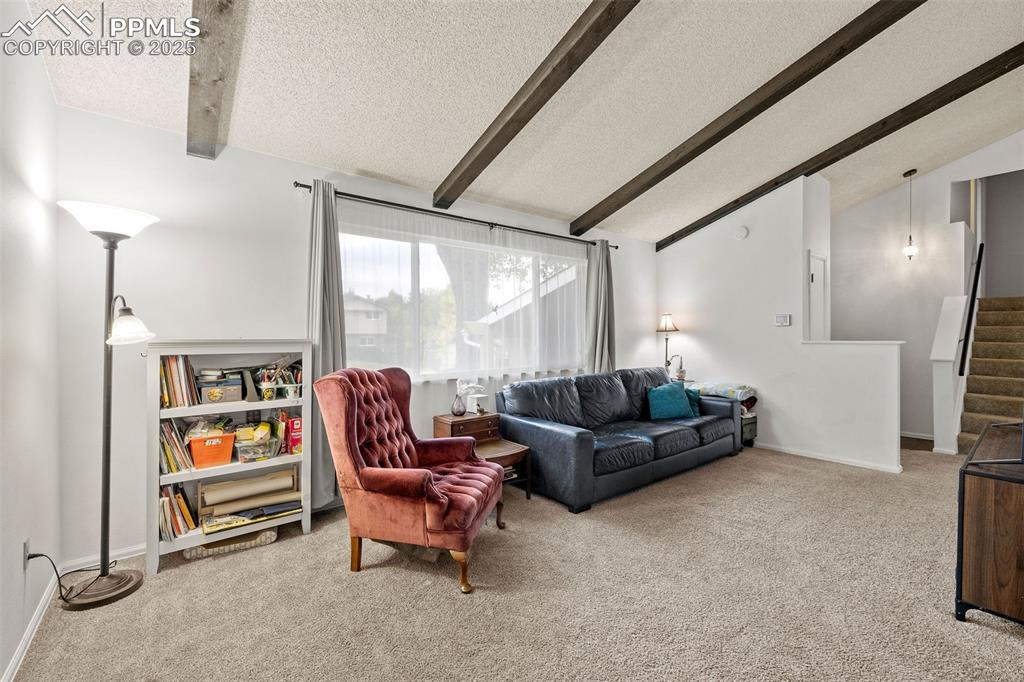 Image 10 of 50: Living area featuring light colored carpet, a textured ceiling, and stairwa