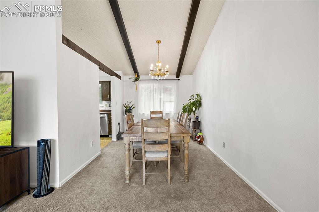 Image 12 of 50: Carpeted dining area featuring beam ceiling and a chandelier