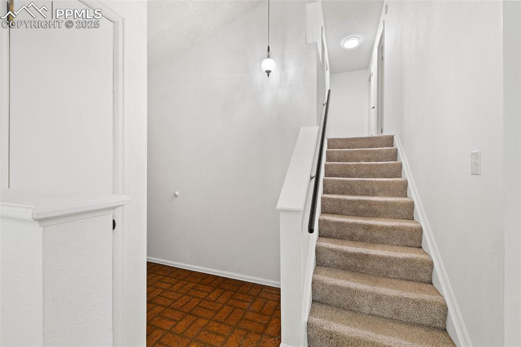 Image 19 of 50: Stairs with brick patterned flooring and a textured ceiling