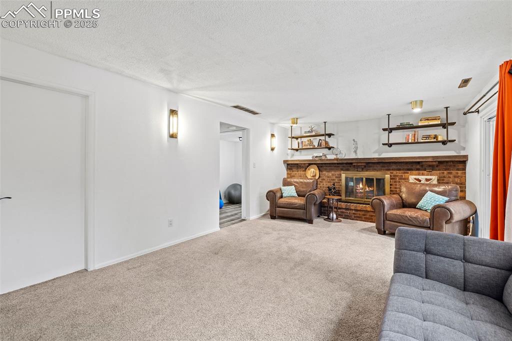 Image 26 of 50: Living area with carpet floors, a fireplace, and a textured ceiling