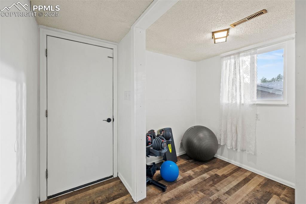 Image 28 of 50: Exercise room featuring a textured ceiling and dark wood-style flooring