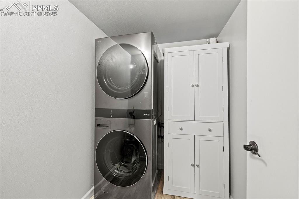 Image 33 of 50: Laundry area featuring stacked washing machine and dryer, cabinet space, an