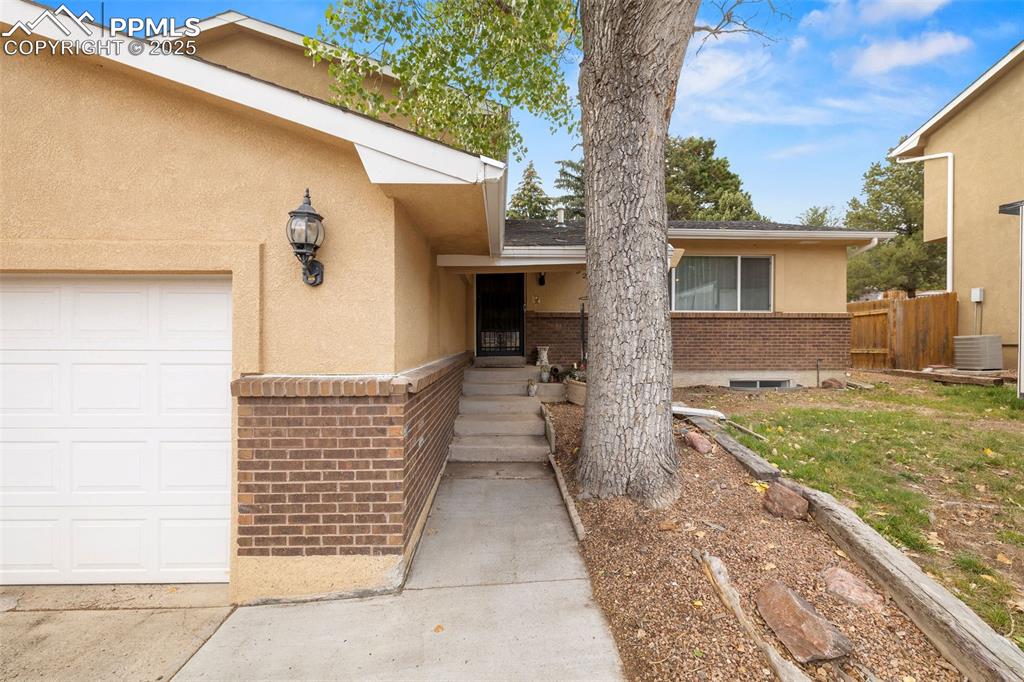 Image 6 of 50: Property entrance with stucco siding, brick siding, and a garage