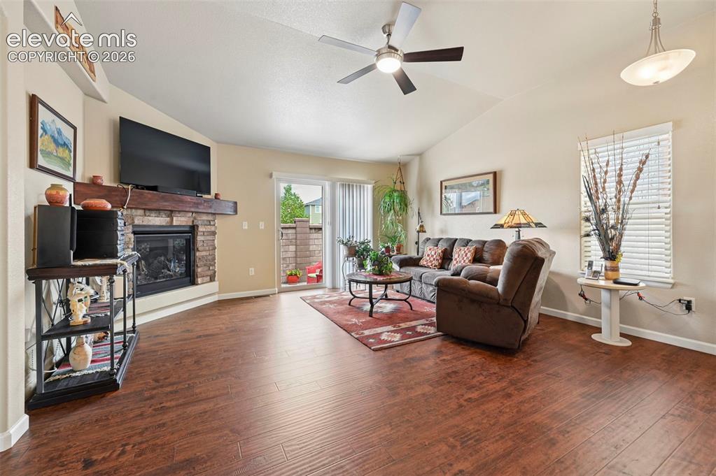 Image 11 of 38: Living room featuring vaulted ceilings, vinyl flooring, a stone fireplace w