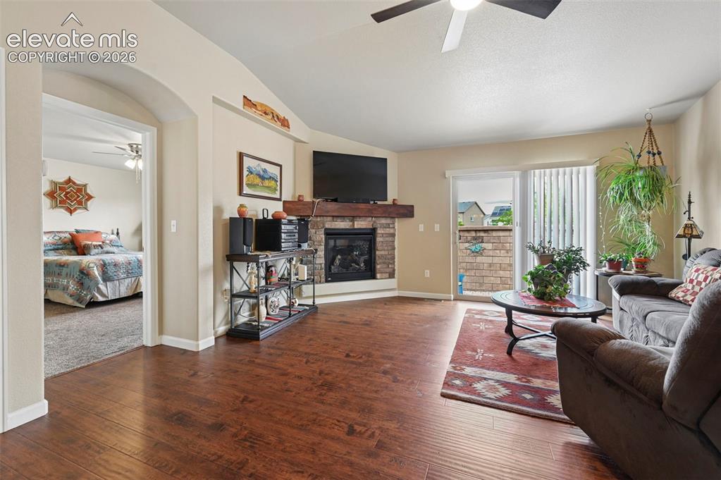 Image 12 of 38: Living room offers a cozy gas fireplace with brick surround and ceiling fan