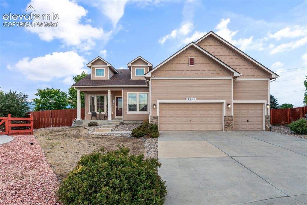 Caption: Two-car garage with stone accents, covered front porch, dormer windows, and a fenced yard with a gat