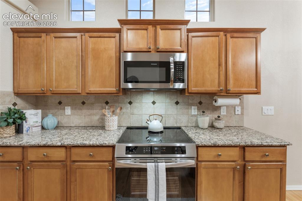 Image 11 of 50: Kitchen featuring wood cabinetry, granite countertops, tile backsplash with