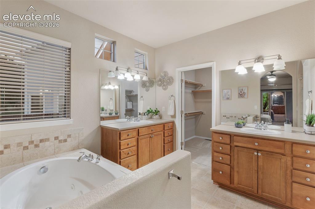 Image 19 of 50: Built-in soaking tub, dual vanity with wood cabinetry, tiled flooring, and