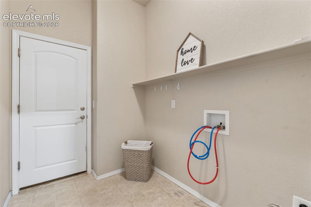 Image 36 of 50: Utility room with a white panel door, light-toned wall paint, and tiled flo