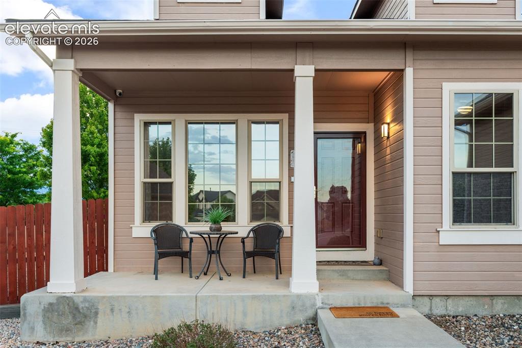 Image 5 of 50: Covered front porch with white columns, light brown siding, a dark red entr
