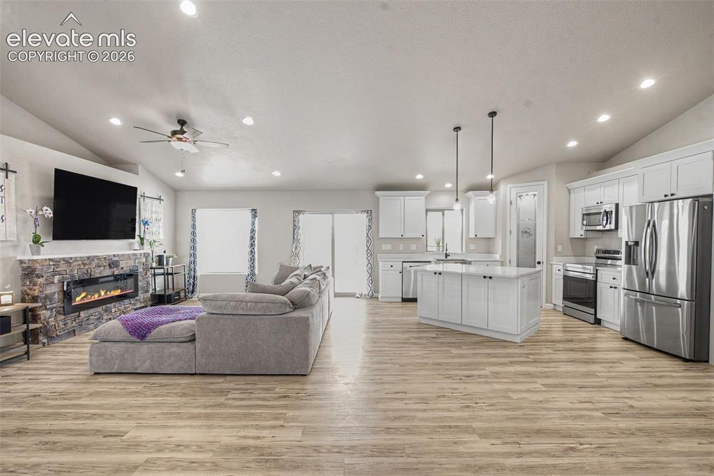 Image 10 of 47: Open-concept living area with wood-finish flooring, vaulted ceilings, and r