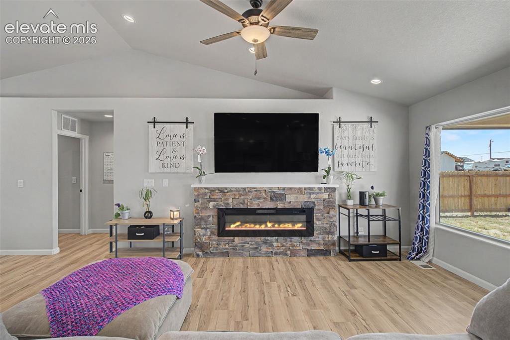 Image 11 of 47: Living area featuring a stone-clad fireplace with an electric insert, vault