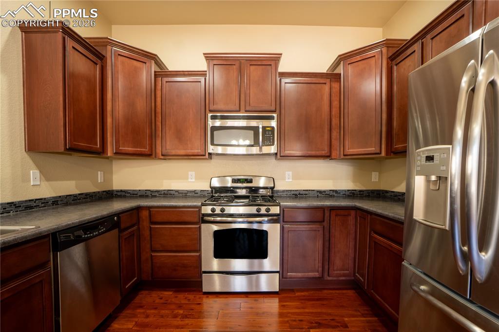 Image 12 of 33: Kitchen with stainless steel appliances, dark countertops, and dark wood fi