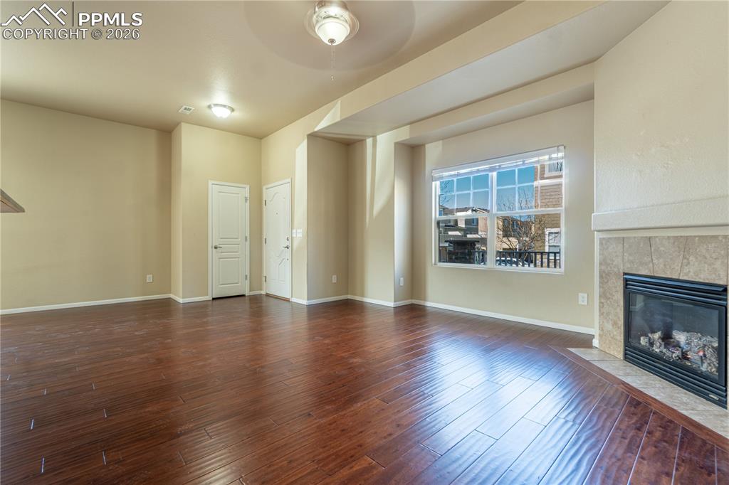 Image 6 of 33: Unfurnished living room with a tile fireplace, a ceiling fan, and dark wood