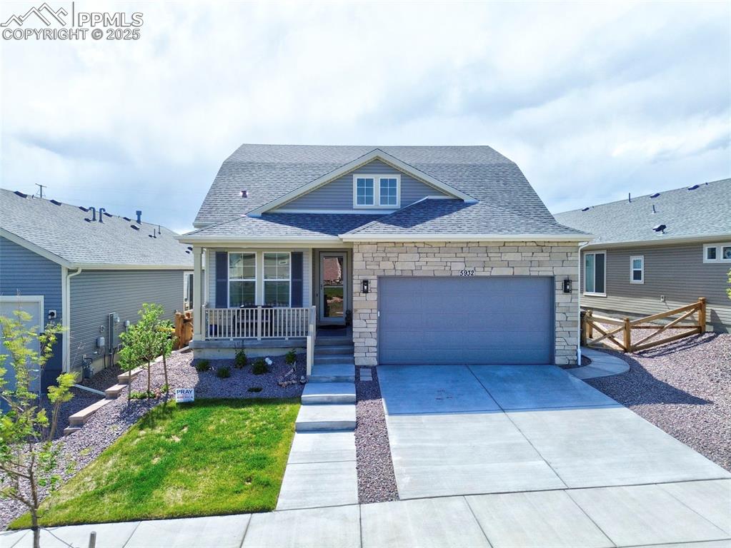 Caption: View of front of property with a porch, roof with shingles, an attached garage, stone siding, and co