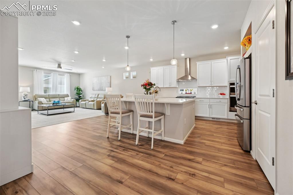 Image 10 of 44: Kitchen featuring wall chimney exhaust hood, freestanding refrigerator, lig