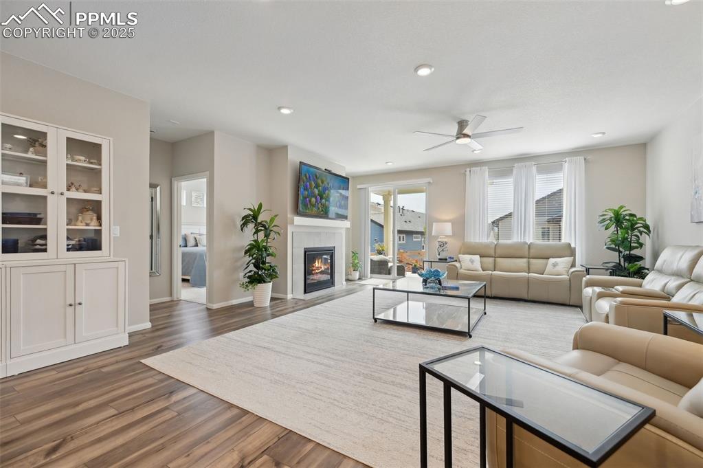 Image 14 of 44: Living room featuring wood finished floors, ceiling fan, a tile fireplace,
