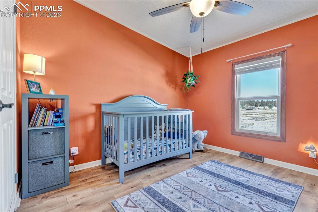 Image 30 of 36: Bedroom featuring a crib, light wood-style floors, and ceiling fan