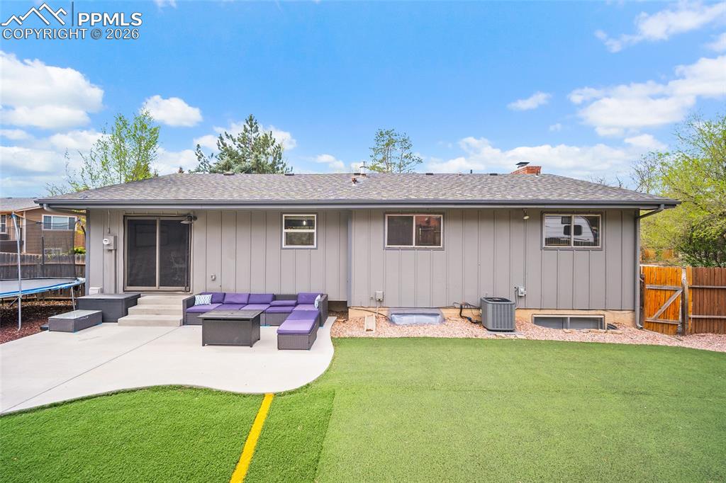 Image 34 of 38: Back of house featuring outdoor furniture, roof with shingles, a trampoline