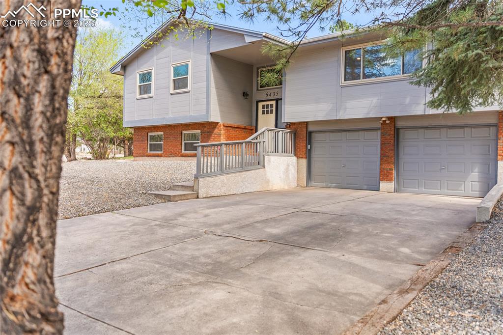 Image 4 of 38: Bi-level home with brick siding, an attached garage, and concrete driveway