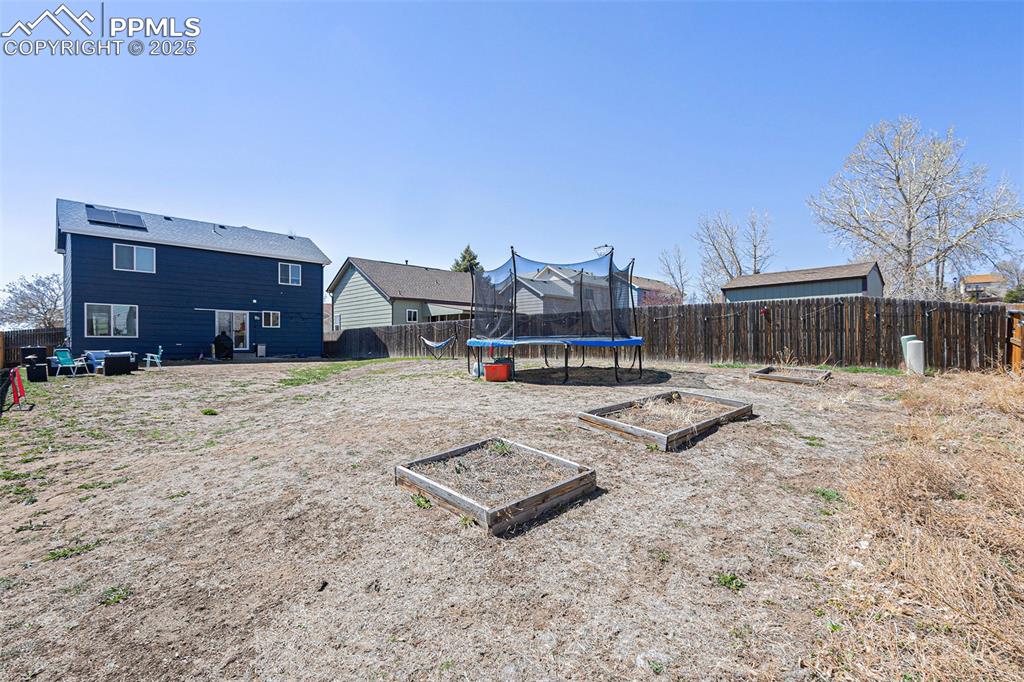 Image 21 of 21: View of yard featuring a fenced backyard, a vegetable garden, and a trampol