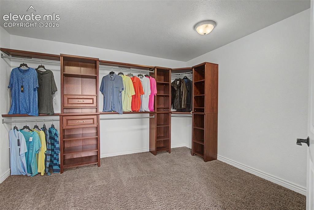 Image 22 of 50: Large walk-in closet featuring custom built-in shelving, drawers, and hangi