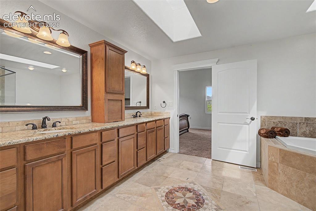 Image 24 of 50: Dual sink vanity with abundant cabinetry, skylight, and natural stone finis