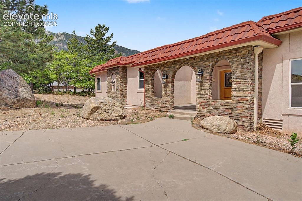 Image 3 of 50: Stone and stucco exterior with mountain foothill backdrop