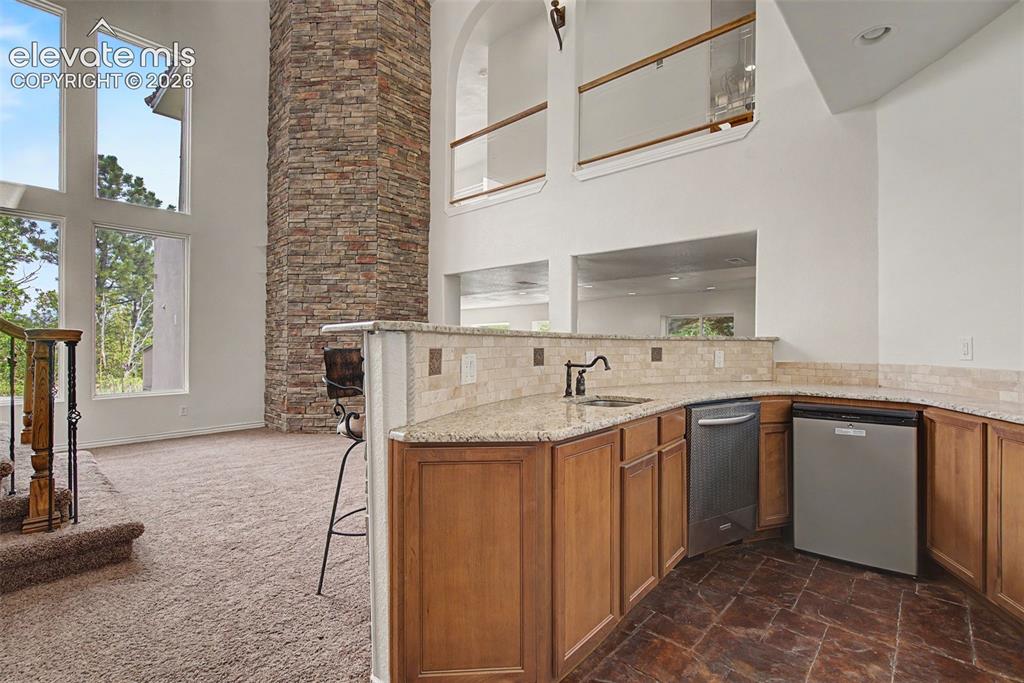Image 33 of 50: Built-in wet bar with seating, sink, beverage refrigerator, and granite cou